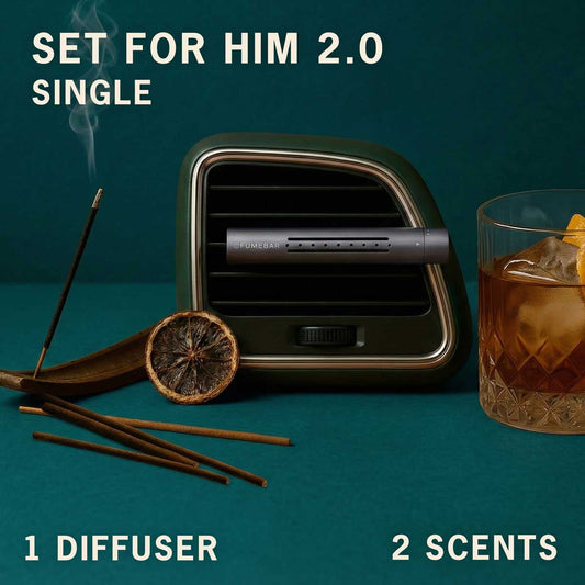 A fragrance diffuser in a car vent with incense sticks and a glass of whisky nearby on a teal studio background, labeled 'Set for Him 2.0 Single' with '1 Diffuser' and '2 Scents'