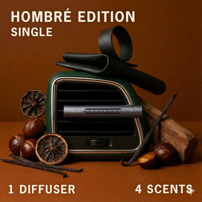 A fragrance diffuser in a car vent with vanilla pods, chestnuts and wood nearby, on a brown studio background, labeled 'Hombre Edition Single' with '1 Diffuser' and '4 Scents'