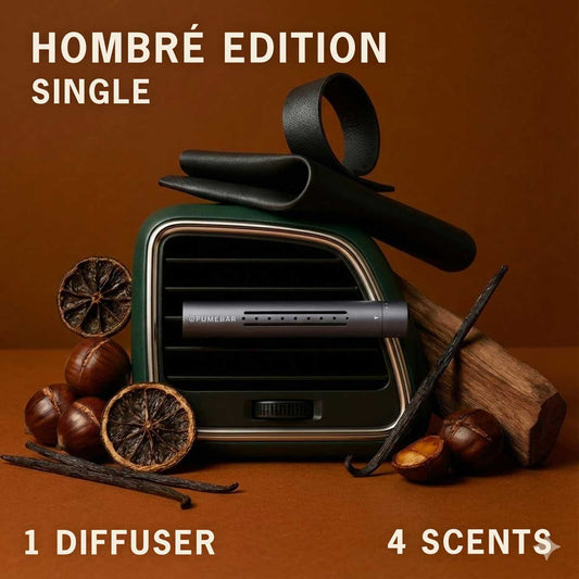 A fragrance diffuser in a car vent with vanilla pods, chestnuts and wood nearby, on a brown studio background, labeled 'Hombre Edition Single' with '1 Diffuser' and '4 Scents'
